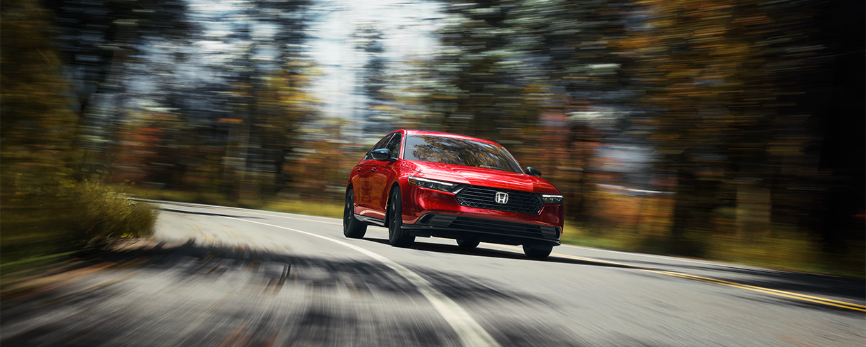 Plan de trois quarts avant d’une Accord rouge qui roule vers la caméra dans un virage sur l’autoroute, dans une forêt tempérée, de jour.